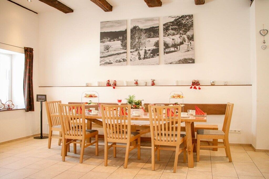 A dining area with wooden chairs and a table, a wall-mounted shelf with decorative items, and a window with curtains.
