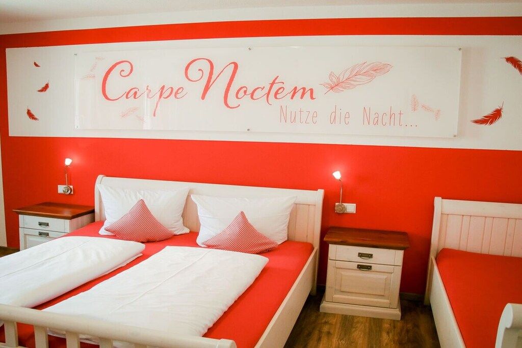 Une chambre d’hôtel aux couleurs rouge et blanc, comprenant un lit double avec une literie rouge et blanche, deux tables de chevet avec des lampes et un panneau décoratif au mur.