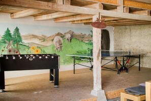 Ein Zimmer mit einem Kicker, einem Pong-Tisch und einem Wandgemälde einer Berglandschaft.