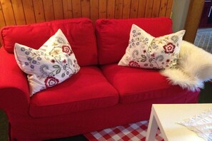 Ein rotes Sofa mit Kissen mit Blumenmuster und einem weißen, flauschigen Gegenstand darauf.