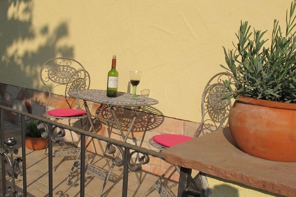 Un balcón con una mesa, sillas, una planta en maceta y una botella de vino.