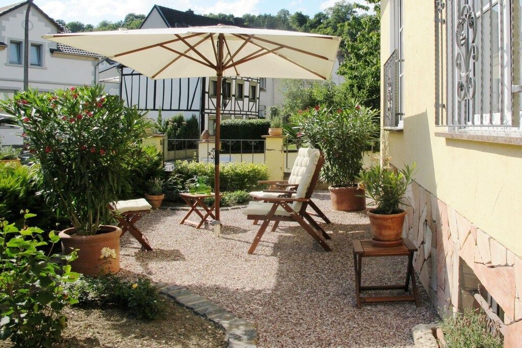 Et udendørs opholdsområde med et bord og stole, omgivet af plantekasser og en stor parasol.