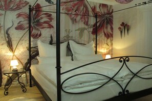 A four-poster bed with a floral wallpaper backdrop, a bedside table with a lamp, and a wall-mounted flower arrangement. - Holiday home in Remagen with swimming pool (Remagen)