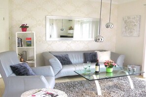 A modern living room with a grey sofa, a glass coffee table, a bookshelf, and a large mirror. - Holiday home in Remagen with swimming pool (Remagen)