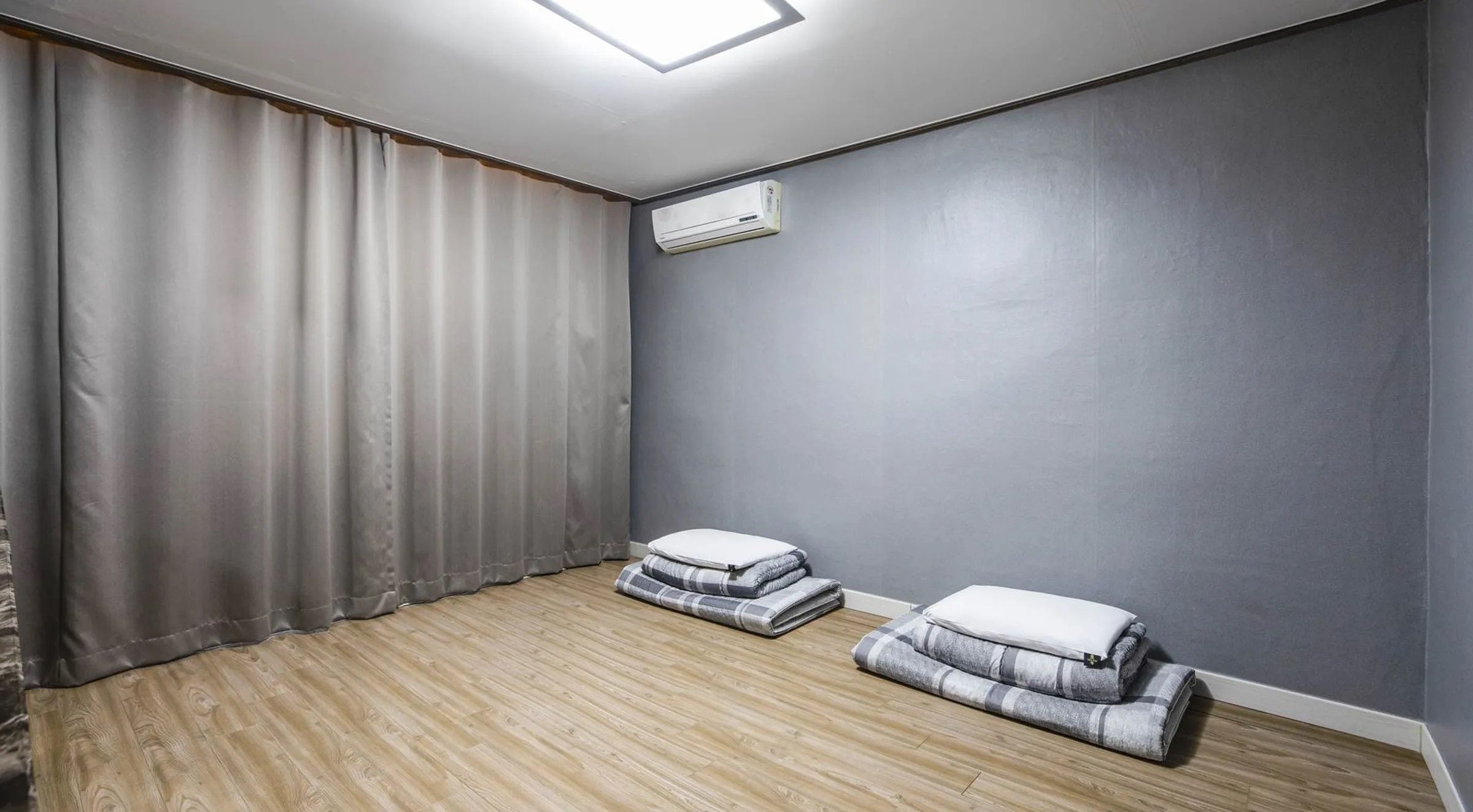 Ein Zimmer mit Holzboden, grauen Wänden, einer Deckenleuchte und einer Klimaanlage.