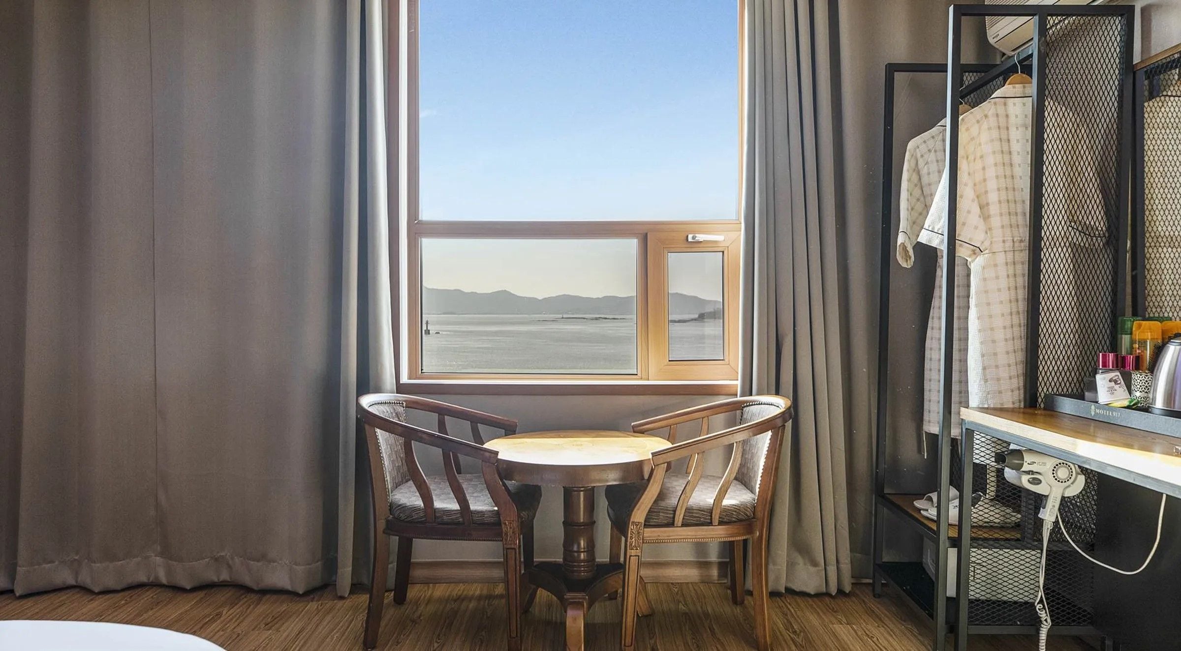 A room with a view of the sea, a table with two chairs, a mirror, and a hairdryer on a shelf.