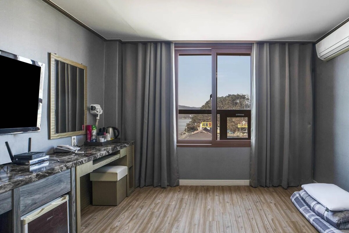 Habitación de hotel con cama, escritorio con televisión de pantalla plana, ventana con cortinas y aire acondicionado.