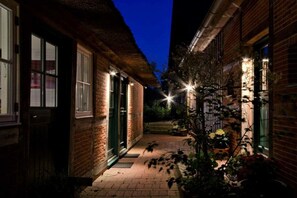 Ein schmaler Backsteinweg führt zu einem Haus mit einem Strohdach und einem kleinen Garten mit Topfpflanzen.