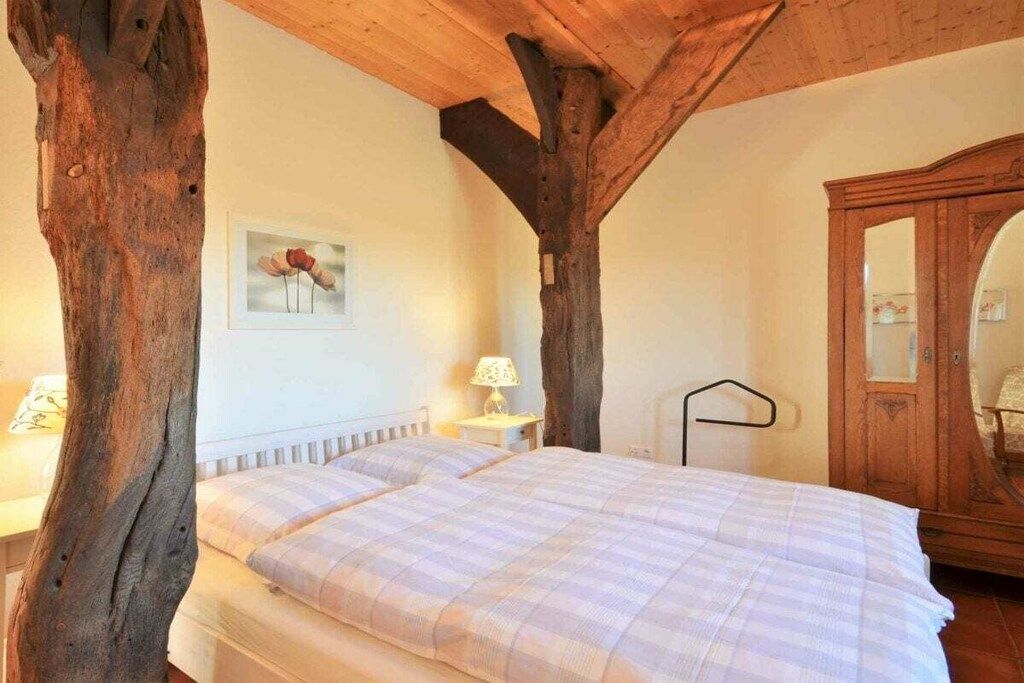 Une chambre avec un plafond en bois, un lit recouvert d’une couverture à carreaux, une table de chevet avec une lampe et une armoire en bois.