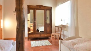 Un dormitorio con un armario de madera, una cama, una silla y una ventana con cortinas.