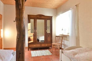 A bedroom with a wooden wardrobe, a bed, a chair, and a window with curtains. - "On the dike" - holiday apartment (Bremen)