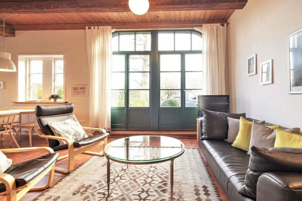 A living room with a sofa, armchairs, a glass coffee table, and a view through a large window.