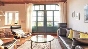 A living room with a sofa, armchairs, a glass coffee table, and a view through a large window.