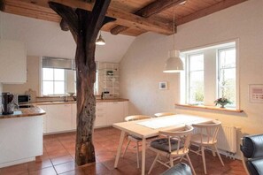 A kitchen with white cabinets, a dining table with chairs, a large window, and a tree trunk in the center. - "On the dike" - holiday apartment (Bremen)