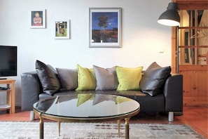 A living room with a sofa, a glass coffee table, and framed pictures on the wall. - "On the dike" - holiday apartment (Bremen)