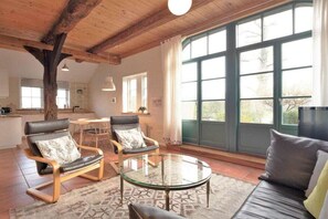 Ein geräumiges Wohnzimmer mit großem Fenster, einem runden Glastisch und zwei Ledersesseln.