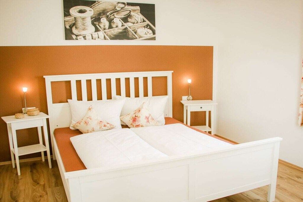 A bed with a white headboard, two bedside tables, and a wall-mounted picture.