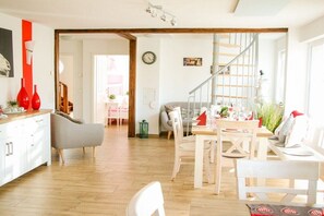 A bright, open-plan living space with a wooden staircase, a dining area with white chairs, and a kitchen with white cabinets. - Holiday home in Hayingen with swimming pool (Hayingen)