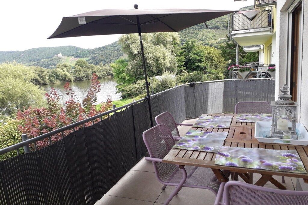 Un balcón con mesa y sillas, con vistas a un río y vegetación.