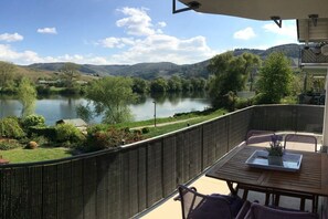 Ein Balkon mit Blick auf einen See und Hügel, ausgestattet mit einem Tisch und Stühlen.