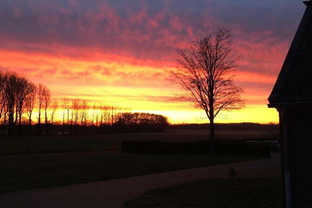 Een zonsondergang boven een landelijk landschap met een pad en bomen.