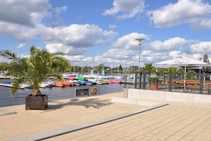 A marina with boats, a palm tree, and a cafe area with outdoor seating. - At the Steenbrukshof woods (Xanten)