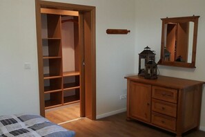 A room with a wooden wardrobe, a small cabinet, a mirror, and a bed with a patterned bedspread. - At the Steenbrukshof woods (Xanten)
