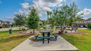 A park with picnic tables and benches, surrounded by trees and a playground. - Near Highways & Hospitals! Extended Stay in Katy (Katy)