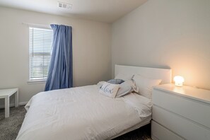 A bedroom with a bed, a bedside table, a lamp, and a window with curtains. - Near Highways & Hospitals! Extended Stay in Katy (Katy)