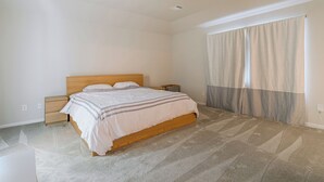 Une chambre à coucher comprenant un lit, des tables de chevet, un ventilateur de plafond et une grande fenêtre avec des rideaux.