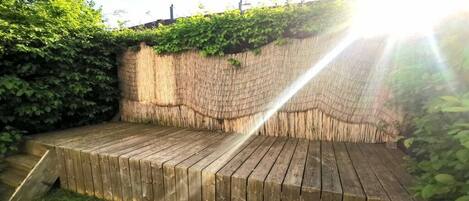 Una terraza de madera con un muro de piedra natural al fondo, rodeada de follaje.