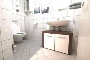 Un bany modern amb un lavabo blanc, dos armaris, un vàter i una zona de dutxa.