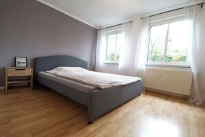 Ein Schlafzimmer mit einem Bett, einem Nachttisch, einem Fenster mit Vorhängen und einer Heizung.