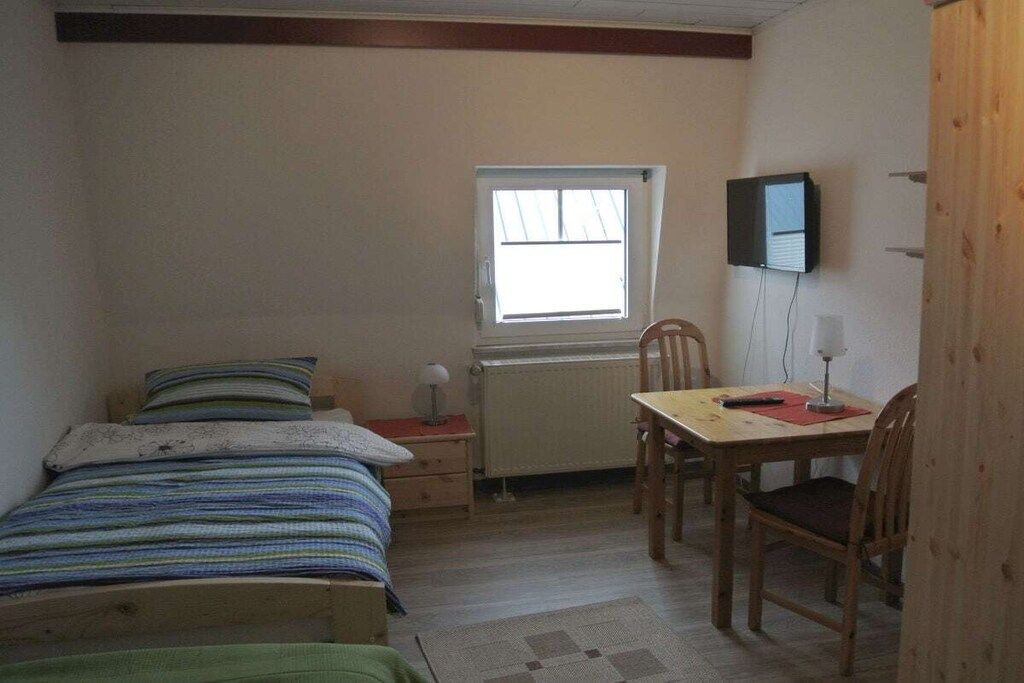 Un dormitorio con cama, escritorio, silla, ventana y televisión.