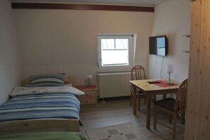 Ein Schlafzimmer mit Bett, Schreibtisch, Stuhl, Fenster und Fernseher.