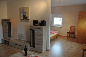 Habitació amb un llit, una cadira, una finestra i un moble de fusta amb alta-parlants.