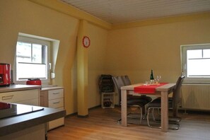 Ein Zimmer mit Esstisch, Stühlen, einer Wanduhr und einem Fenster.