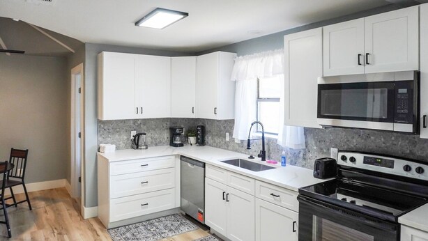 A modern kitchen with white cabinets, a black stove, a microwave, and a coffee maker. - West Oak House - Bright 3-Bedroom Single-Family Home in Wylie (Wylie)