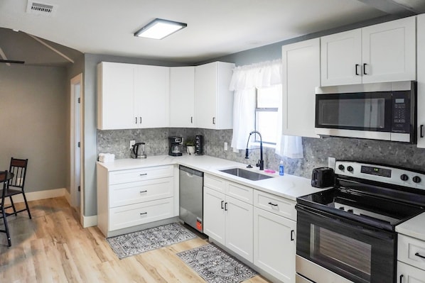 A modern kitchen with white cabinets, a black stove, a microwave, and a coffee maker. - West Oak House - Bright 3-Bedroom Single-Family Home in Wylie (Wylie)