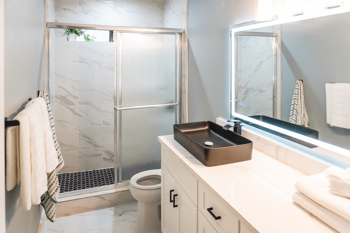 A modern bathroom with a glass shower enclosure, a white toilet, and a black sink with a marble countertop.