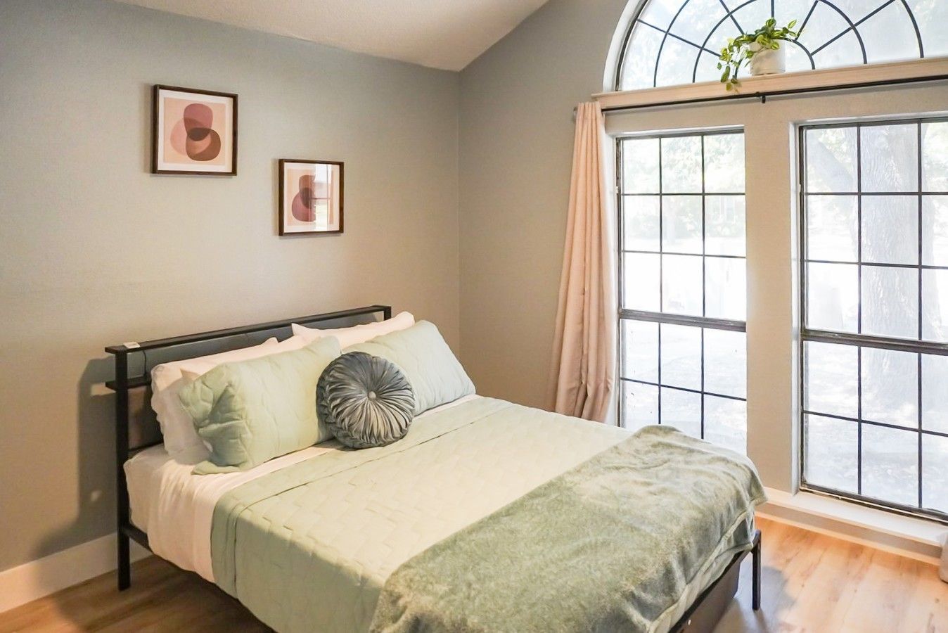 A bedroom with a bed, a window with curtains, and two framed pictures on the wall.