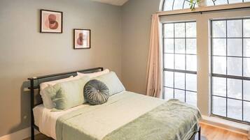 A bedroom with a bed, a window with curtains, and two framed pictures on the wall.