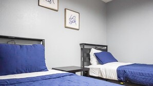 A room with two beds, each with a blue blanket and pillow, a small bedside table, and a wall-mounted picture frame. - West Oak House - Bright 3-Bedroom Single-Family Home in Wylie (Wylie)