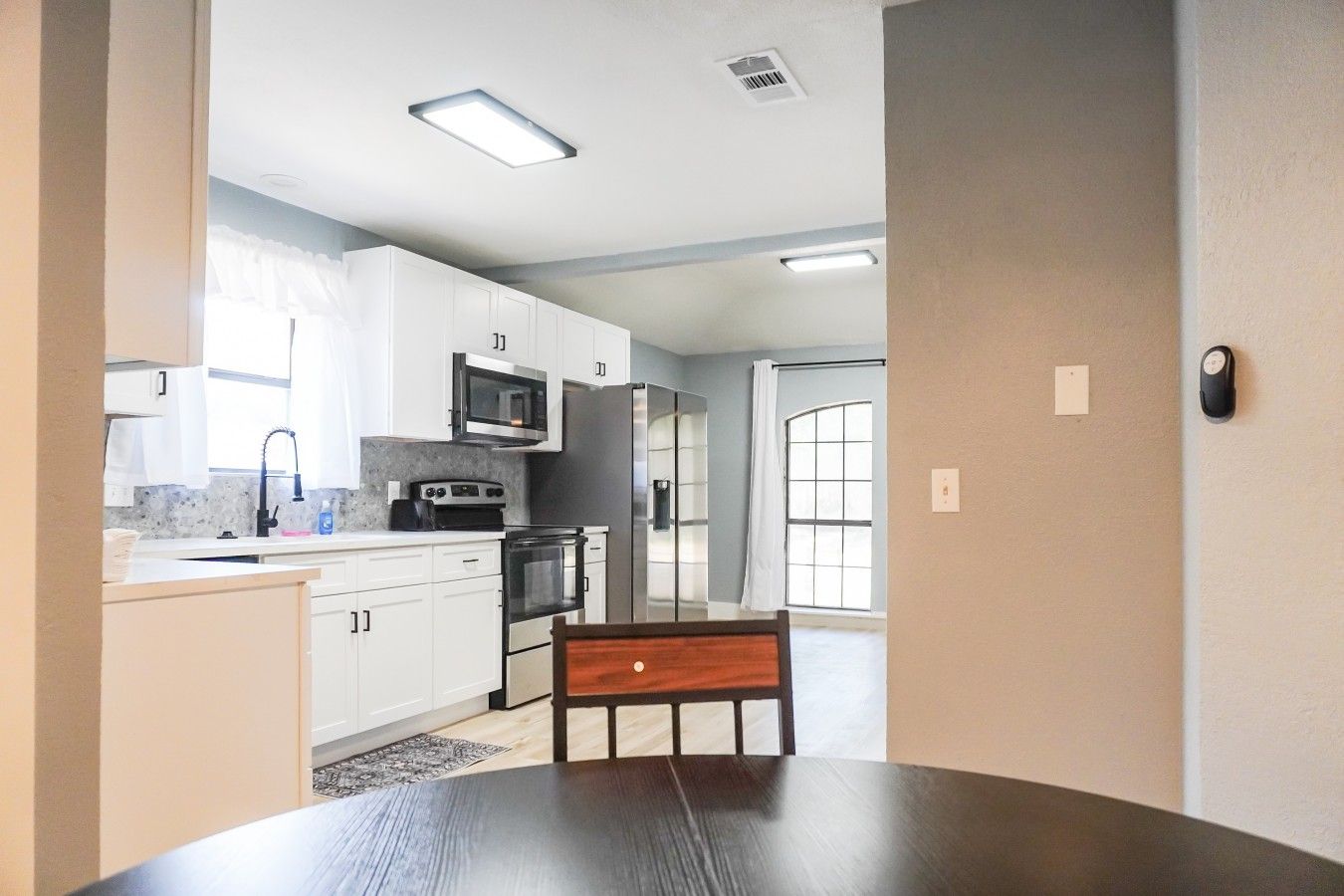 Una cocina moderna con armarios blancos, microondas, estufa y una mesa de comedor con una silla.