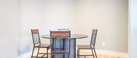 Un coin repas comprenant une table ronde et quatre chaises, avec un design moderne caractérisé par des structures métalliques et des assises en bois.