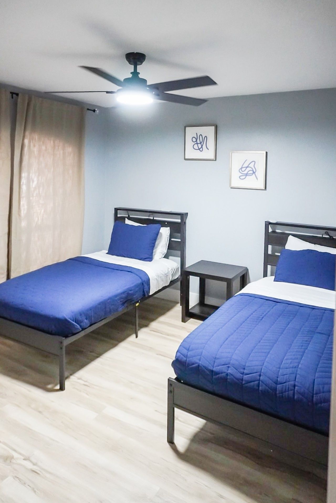 Una habitación con dos camas individuales, un ventilador de techo y una mesita pequeña.
