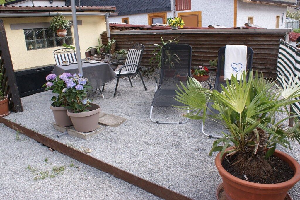 A patio area with a table and chairs, potted plants, and a wooden fence.