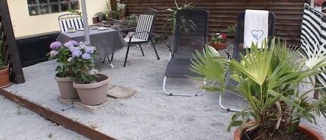 Una zona patio con tavolo e sedie, piante in vaso e una recinzione in legno.