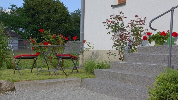 Un escalier extérieur menant à un bâtiment, avec une chaise en métal et une table agrémentée de coussins rouges au premier plan.