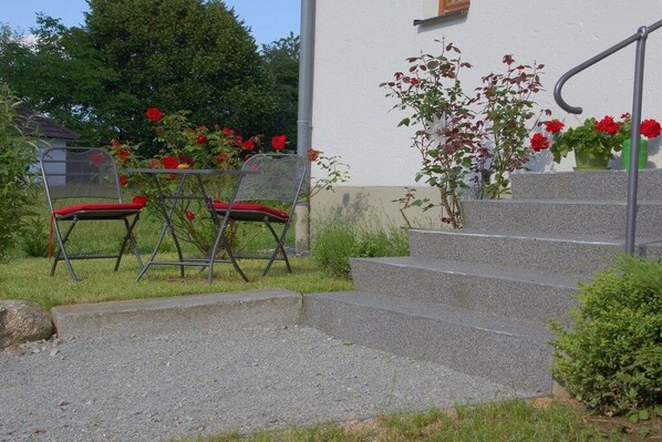 A set of outdoor stairs leading to a building, with a metal chair and a table with red cushions in the foreground. - Panoramic view of the Höllbach valley (Rettenbach)
